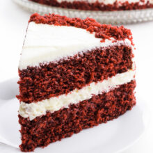 A slice of red velvet cake sits in front of the rest of the cake.