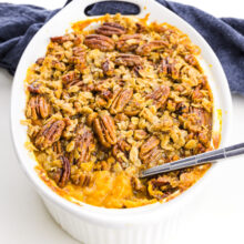A casserole holds sweet potato casserole and a spoon has dished out some of it.