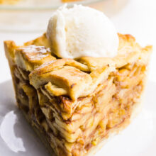 A slice of vegan apple pie has a scoop of ice cream on top and the rest of the pie behind it.