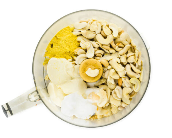 Cashews and other ingredients are in the bowl of a food processor.