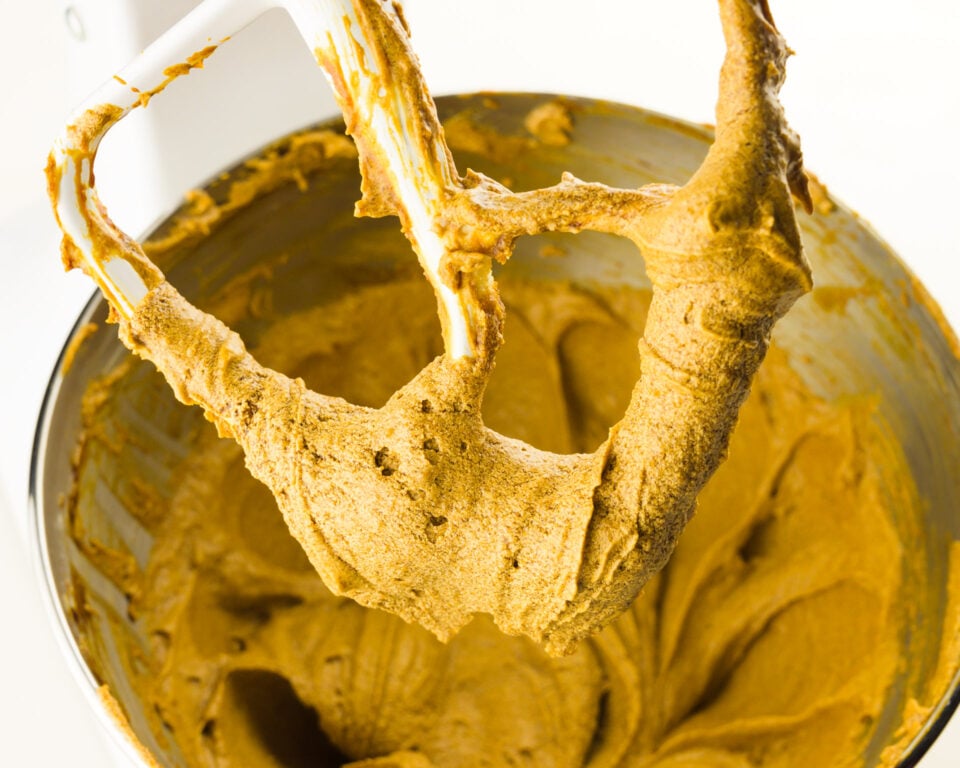 A stand mixer beater has gingerbread cookie batter on it with the bowl of batter below it.