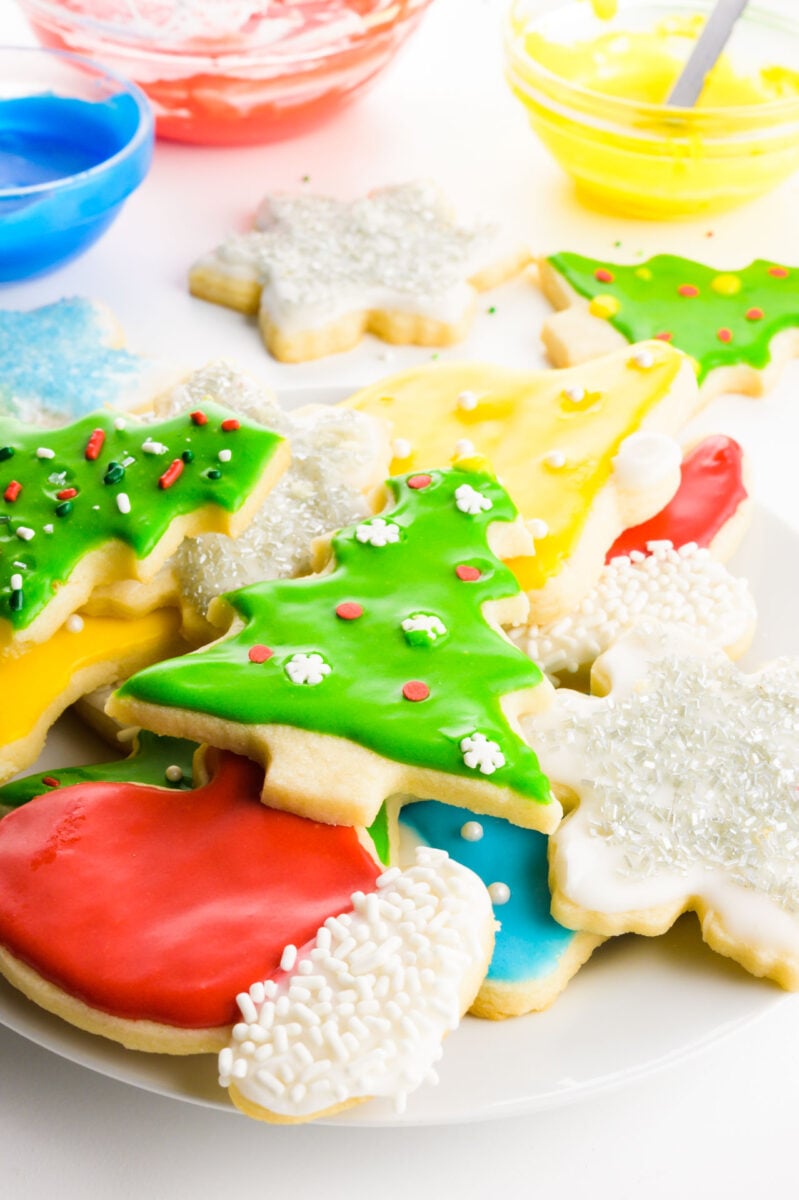 A plate of Christmas decorated sugar cookies sits near bowls of colored icing.