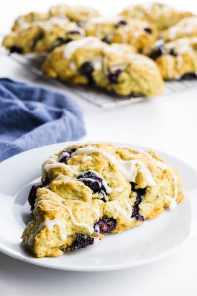 A scone sits on a plate with more vegan scones behind it.