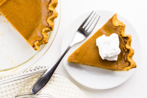 A slice of pie has a fork beside it and the rest of the pie is next to it too.