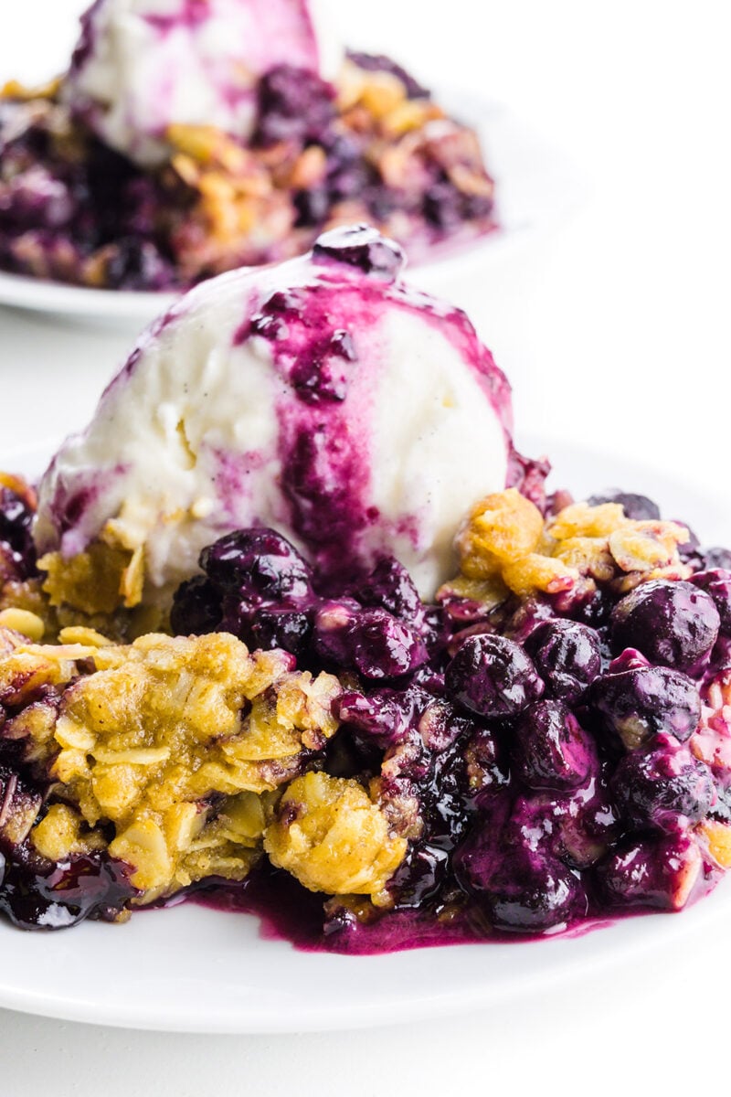 Two plates full of blueberry crumble sit one in from t of the other.