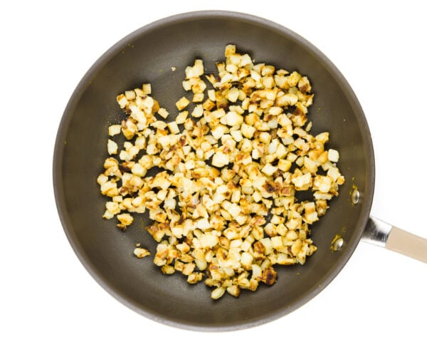 A skillet holds hash browns being cooked.