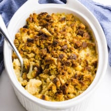 A spoon rests in a casserole dish full of cauliflower gratin. A blue towel is behind it.