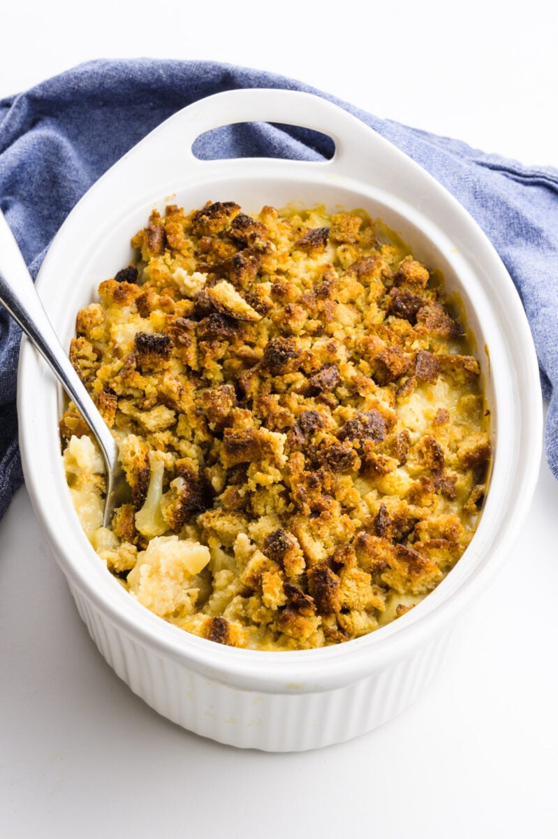 A spoon rests in a casserole dish full of cauliflower gratin. A blue towel is behind it.