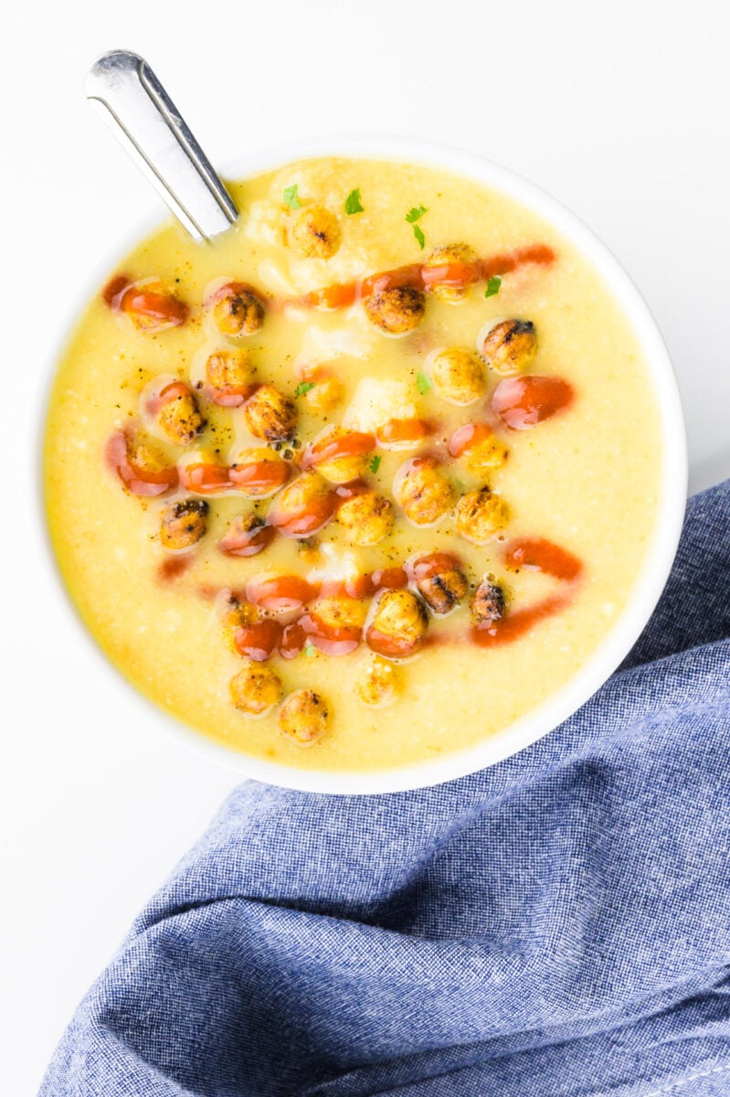 A bowl of soup has croutons in it and drizzles of hot sauce.