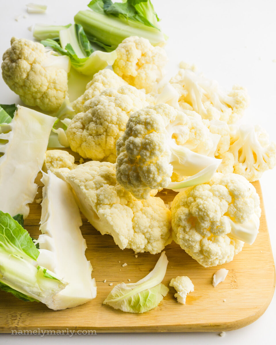Cauliflower florets on a cutting board, along with the stems of the cauliflower.