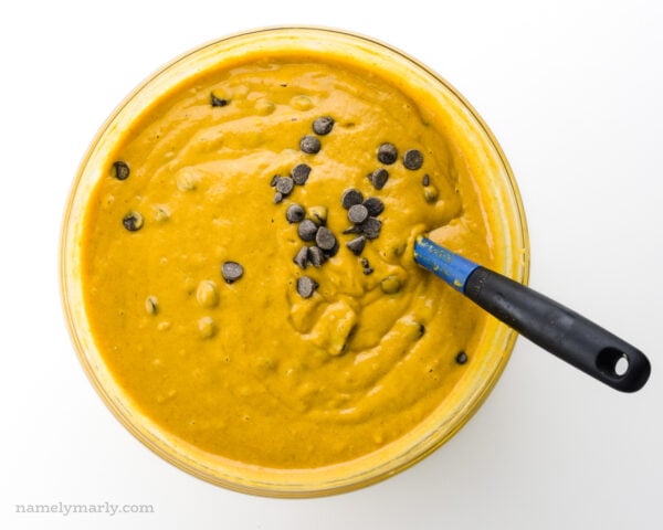 Batter is in a glass bowl showing chocolate chips on top and a spatula for stirring.