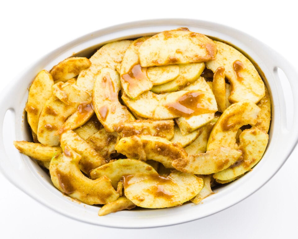 Sliced apples covered in a cinnamon sauce are in a baking dish.