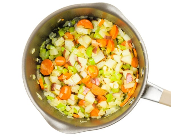 Looking down on a saucepan full of chopped onions, carrots, and celery.