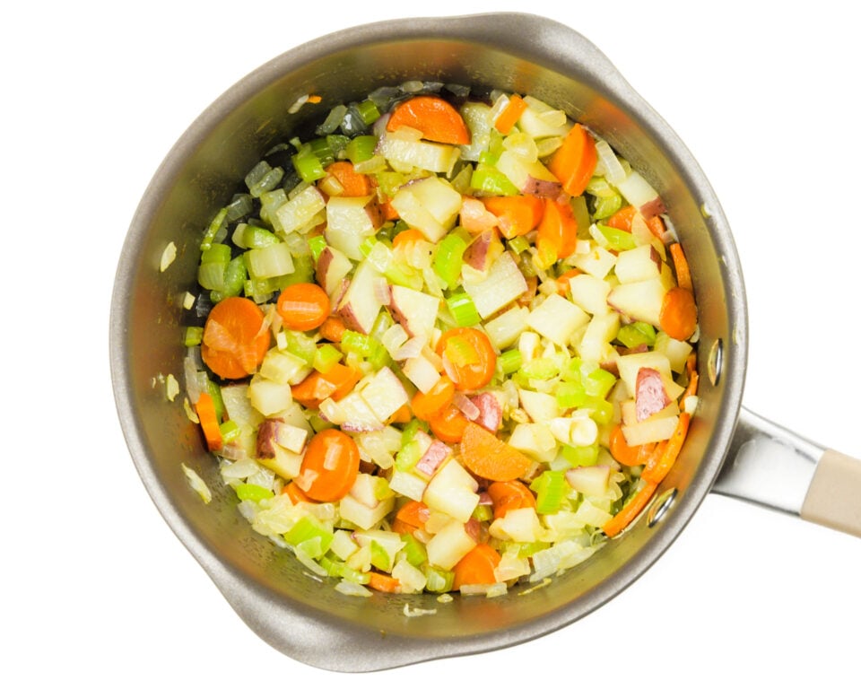 Looking down on a saucepan full of chopped onions, carrots, and celery.