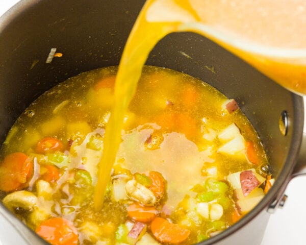 Broth is being poured into a pot full of veggies.