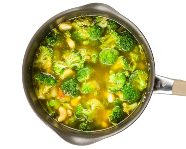 Looking down on a saucepan full of broth, cashews, broccoli, and other veggies.