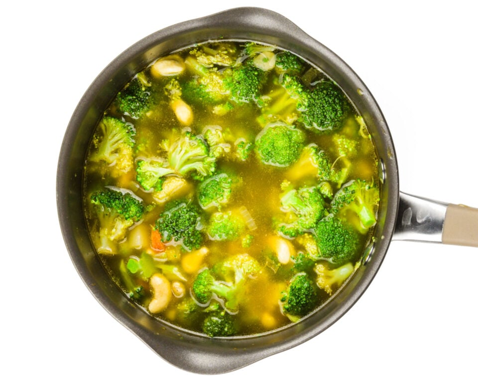 Looking down on a saucepan full of broth, cashews, broccoli, and other veggies.