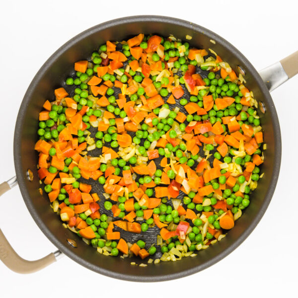 A skillet holds a mixture of vegetables, including peas, carrots, and red bell peppers.