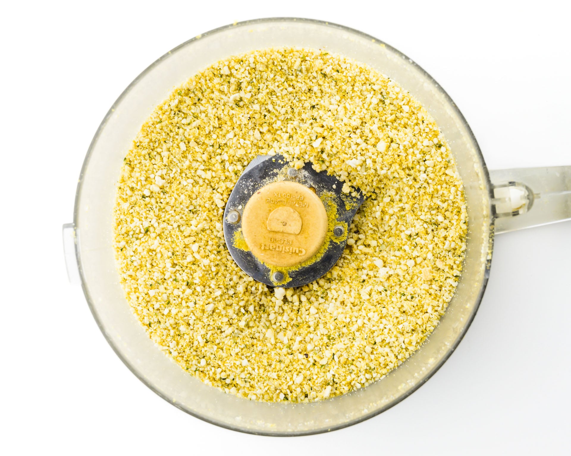 Looking down on a food processor bowl full of grated cashews combined with spices.