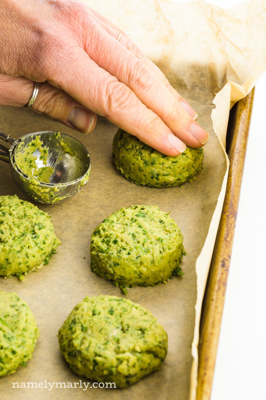 A hand flattens falafel balls into patties.
