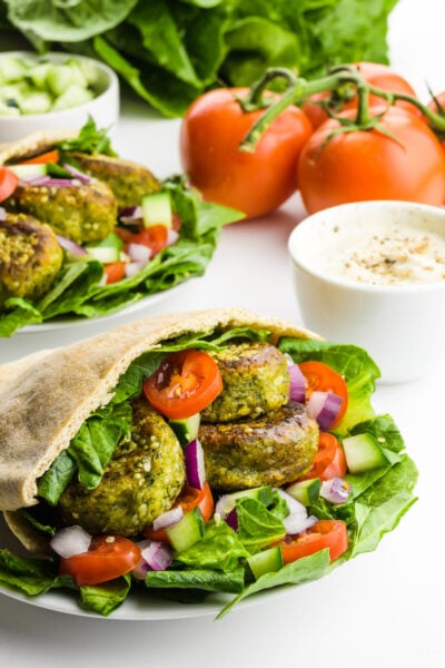 A pita is stuffed full of falafel, greens, chopped tomatoes and more to make a Falafel Sandwich. Other ingredients are behind it.