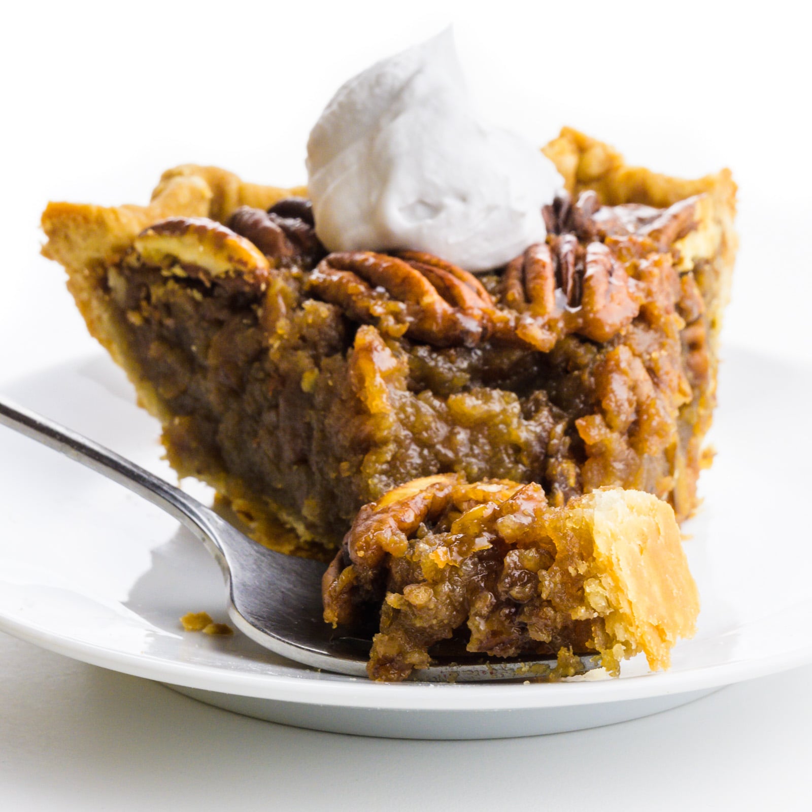 Looking at a slice of pie with whipped cream on top and a fork holding a bite in front of it.