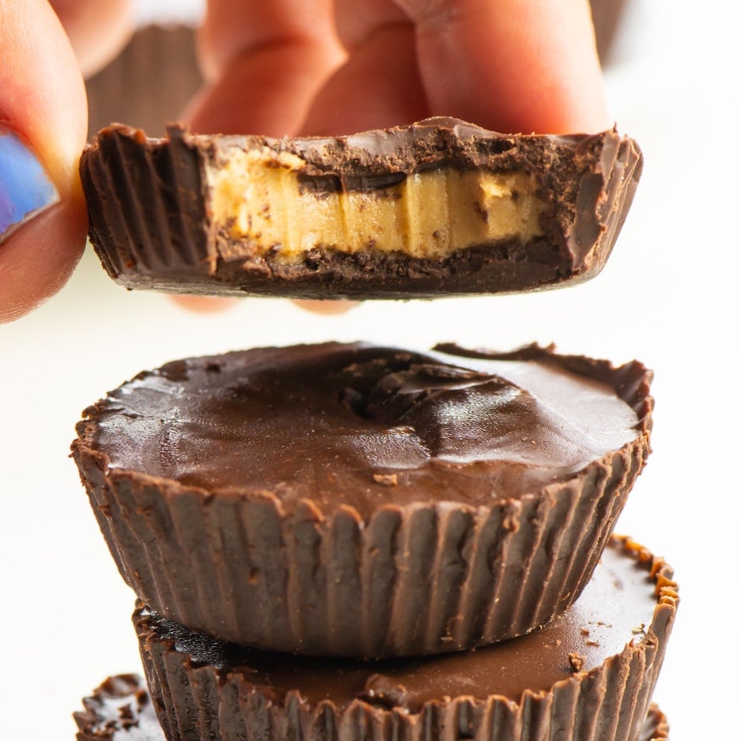 A hand holds a peanut butter cup with a bite taken out of it. It's held over a stack of more candies.