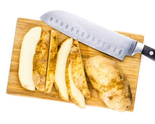 Cut up russet potatoes on a cutting board with a knife.