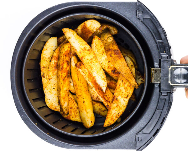 Season potato wedges are in an air fryer basket.