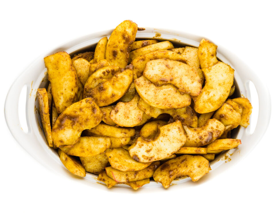 A casserole dish is full of sliced apples covered with cinnamon. 