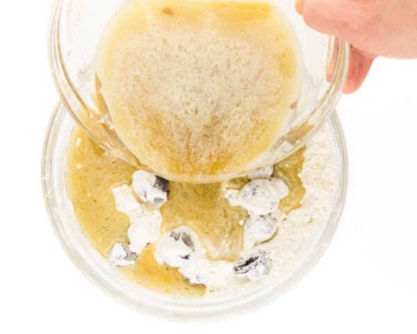 A hand holds a bowl pouring wet ingredients into a bowl of flour ingredients.