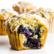 Cherry muffins, one with a bite taken out, sit on a white counter.