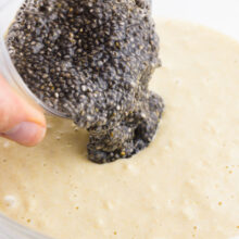 A bowl full of wet chia seeds, referred to as a chia egg, is being poured into batter.