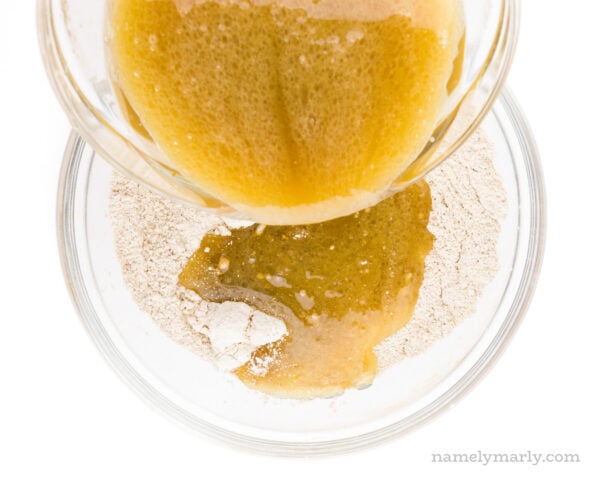 A bowl full of liquid ingredients is being poured into a bowl full of flour ingredients.
