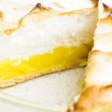 A lemon meringue pie has a slice cut out, showcasing layers of lemon curd and meringue on top.