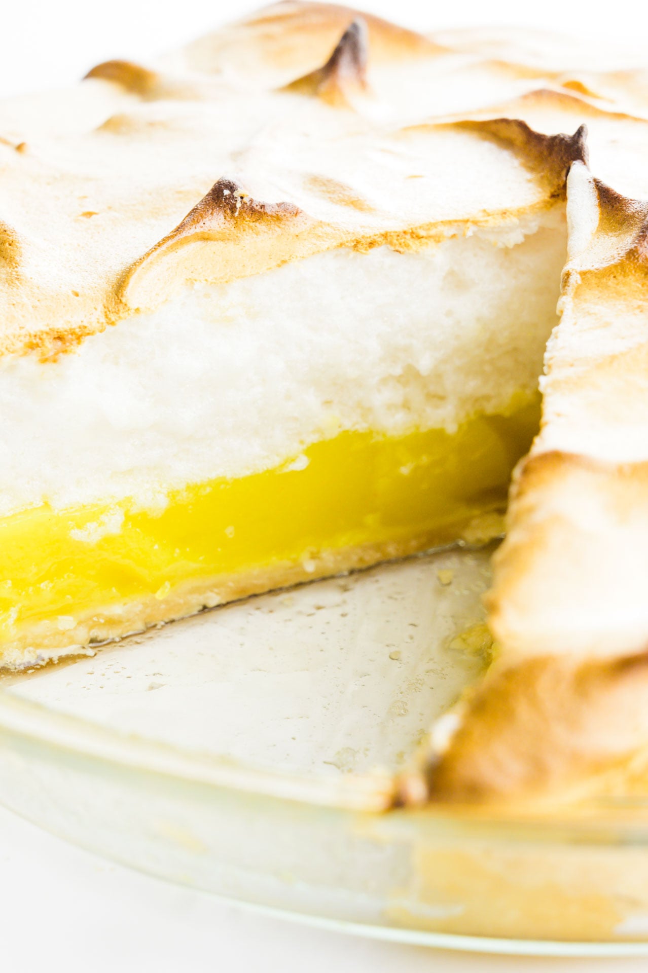 A lemon meringue pie has a slice cut out, showcasing layers of lemon curd and meringue on top.
