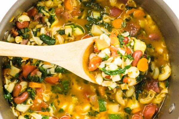 A wooden spoon reaches in to a pot and holds some soup.