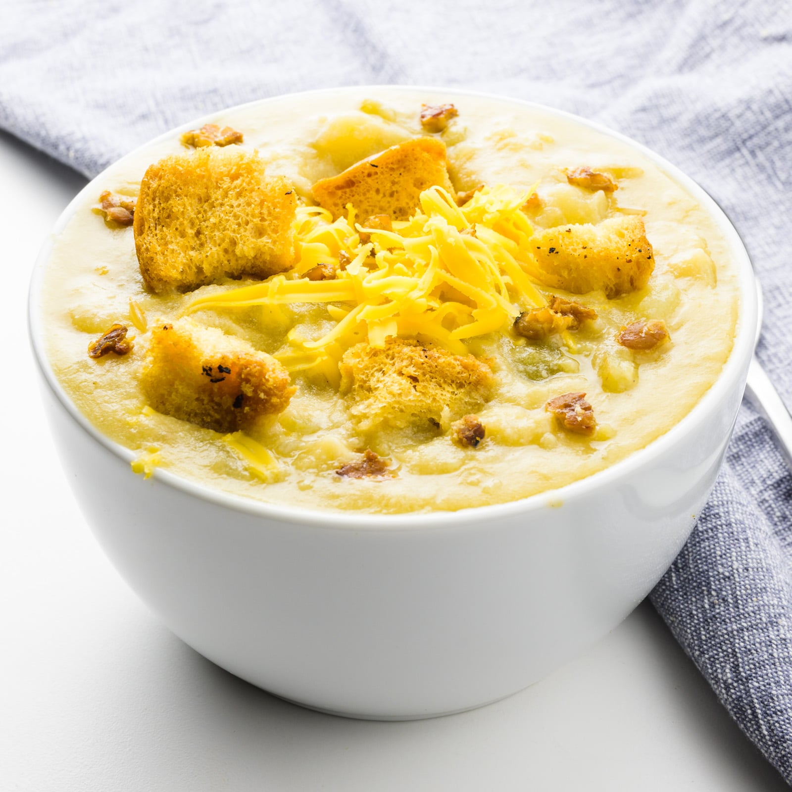 A bowl of vegan potato soup sits next to a grey cloth napkin.