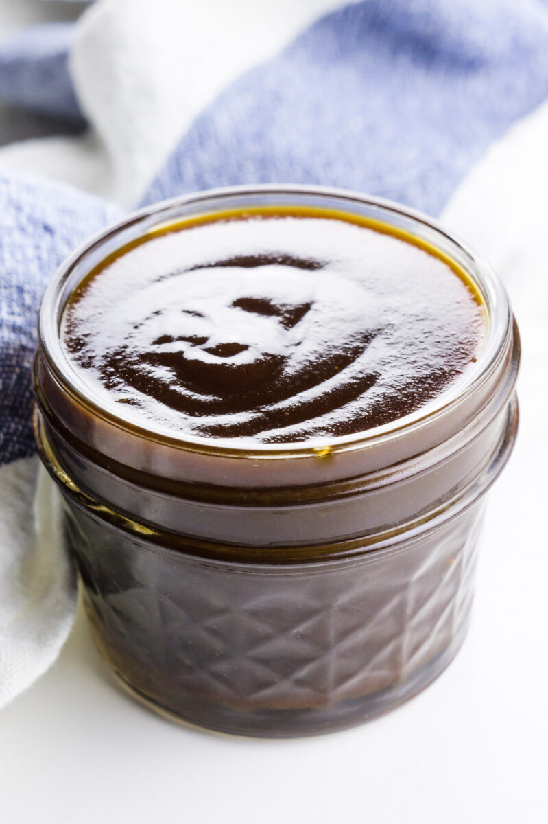 A small mason jar is full of vegan caramel sauce. A blue striped kitchen towel is behind it.