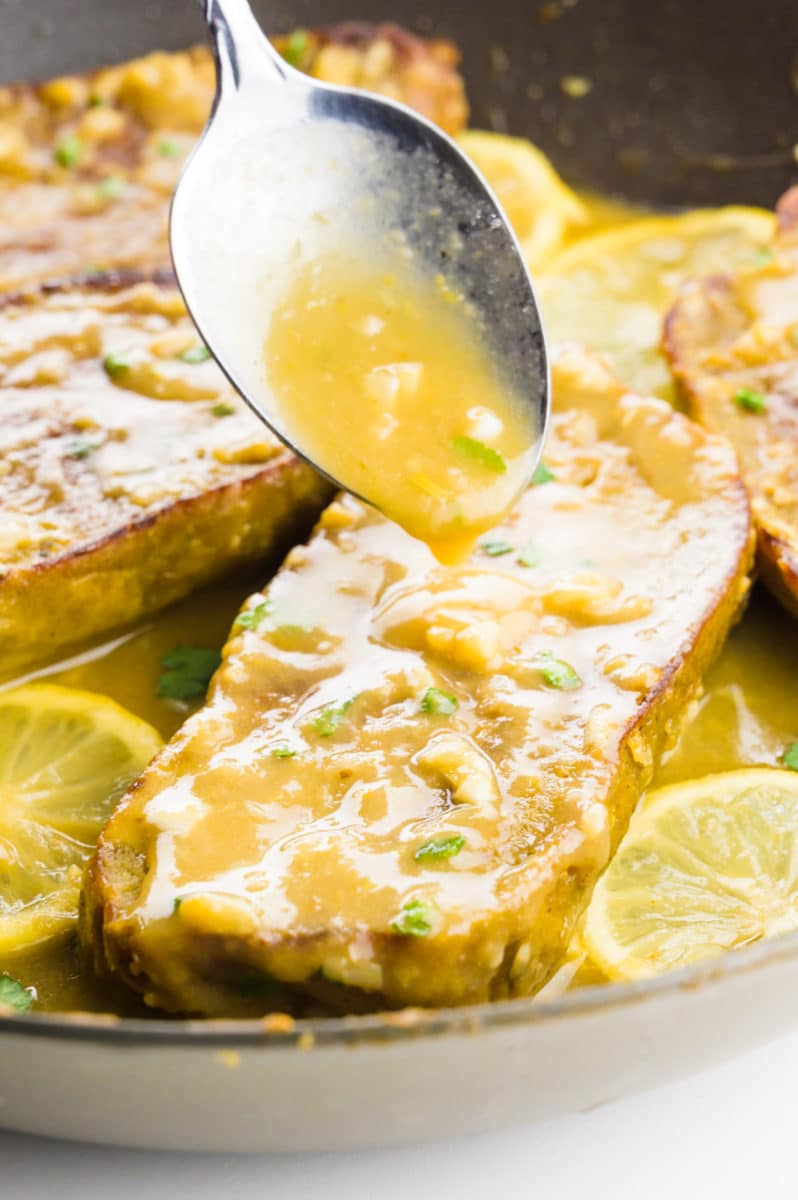 A spoon drizzles sauce over vegan chicken in a skillet.
