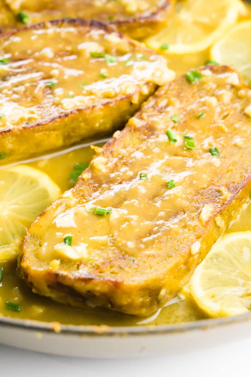 A vegan chicken fillet with sauce over the top next to lemon slices.