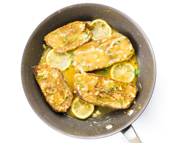 Looking down on a skillet with vegan fillets with gravy and lemon slices.