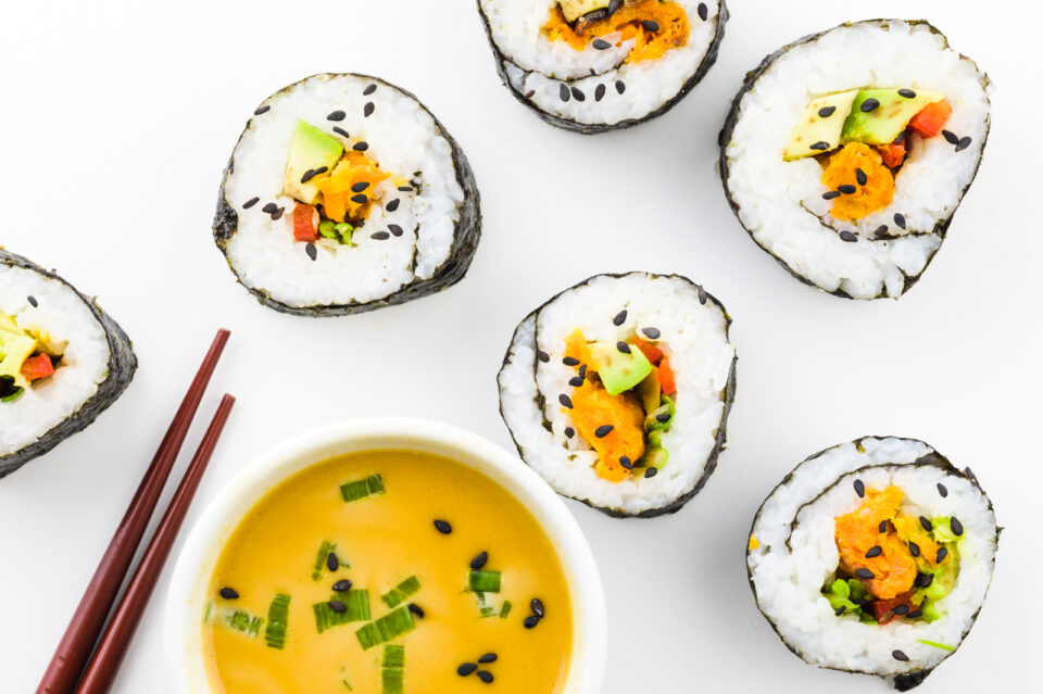 Looking down on several sushi rolls sitting next to a bowl of sauce and chopsticks.