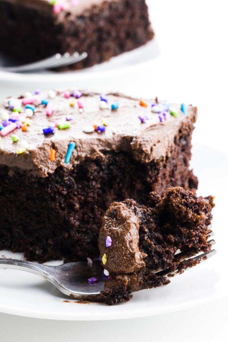 A slice of chocolate wacky cake has a fork with a bite taken out sitting in front of it. There's another slice sitting behind it.