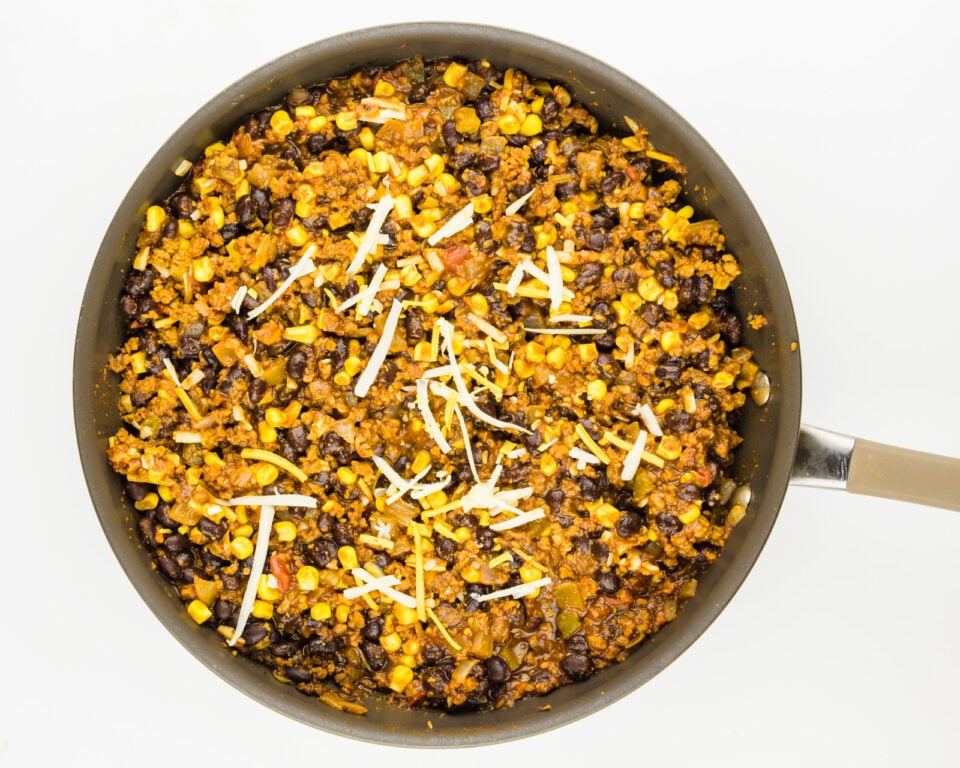 A skillet is full of beans and other ingredients to make vegan taco casserole.
