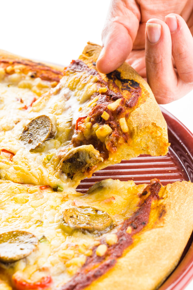 A hand holds a piece of pizza, pulling it out from a pan full of more pizza.