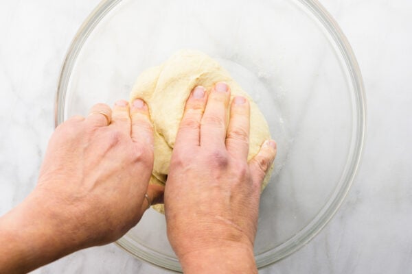 Two hands reach into a glass bowl, kneading some dough.