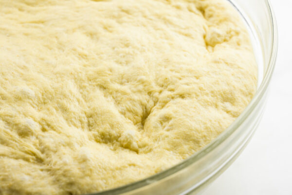 Dough has risen in a glass bowl and this photo shows how it now fills up the bowl to the edges.