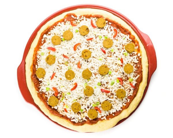 Looking down on an unbaked pizza on a red pizza stone.