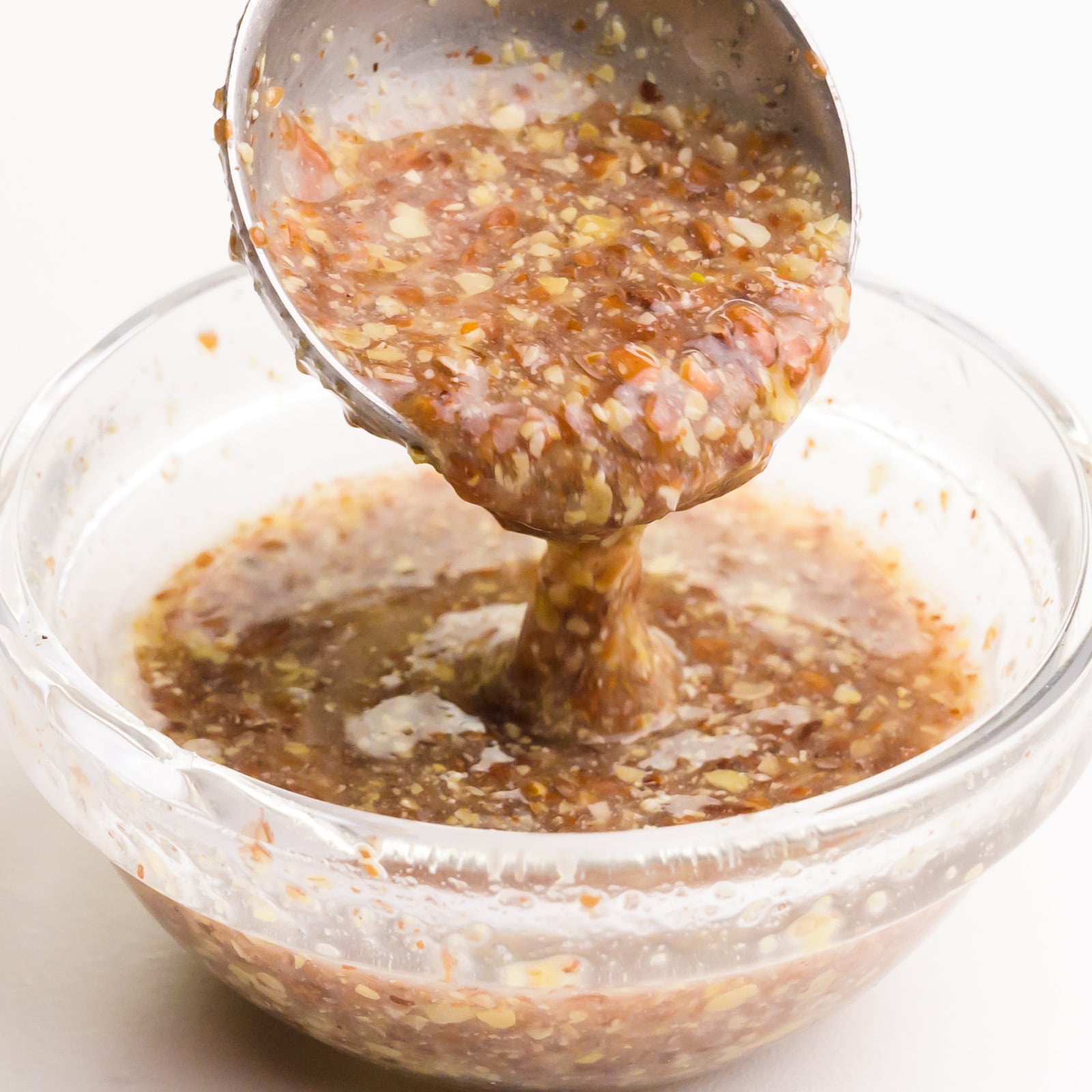 A measuring spoon drizzles a flax egg mixture into a small glass bowl